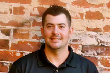 A white man in a black polo t-shirt smiling