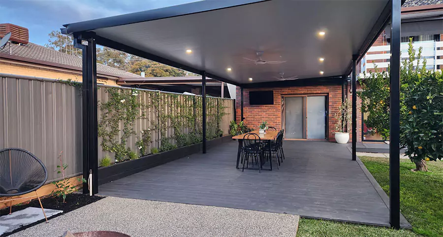 Modern outdoor patio extension with a sleek black roof, recessed lighting, and a dining area, enhancing backyard living space for homeowners.