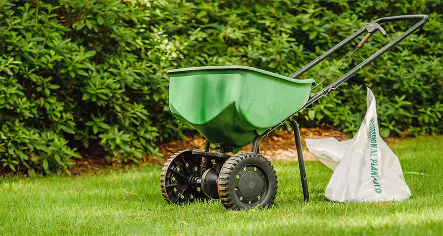 Lawn fertilizer spreader and bag of grass seed on a green lawn—illustrating essential tools for proper lawn seeding and fertilization in Prosper, North Texas