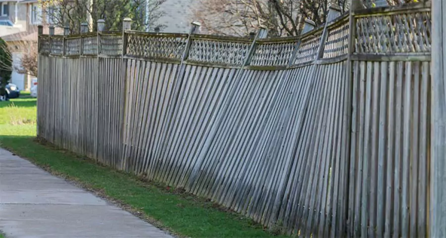 Leaning wooden fence with damaged posts in a residential area, indicating potential structural issues