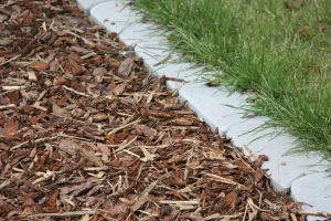 Close-up view of fresh mulch beside a stone landscape border and neatly trimmed grass.