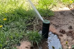 sprinkler head leaking water causing muddy puddle in lawn indicating irrigation system leak and drainage issue in residential yard